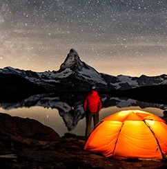Bild: beleuchtetes Zelt an einem See in den Bergen